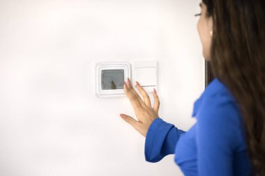 Genç Hintli müşteri kadın klimayı çalıştırmak için kontrol paneli kullanıyor, evdeki termostatı düzenliyor, konaklama sıcaklığını ayarlıyor, duvardaki düğmelere basıyor