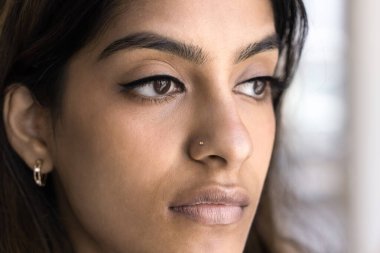 Çizgili gözlü, makyajlı ve burnu açık genç Hintli bir kadın derin düşüncelere dalıp kozmetik cerrahi promosyonuyla yüz portresi çektirmek için poz veriyor.