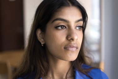 Düşünceli genç Hintli kadın yüz portresi. Düşünceli, 20 'li yaşlarda, göz makyajı ve burun piercingli yakın çekim için kapalı alanda poz veren, başka yöne bakan, sorunları düşünen bir kız.