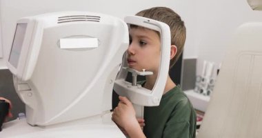 Otomatik görme muayenesinden geçen yakışıklı çocuğu klinikteki otomatik fraktör makinesiyle kapatın. Modern tanı teknolojisi kullanan genç, profesyonel göz doktoru hizmetleri için göz bakımı kontrolü