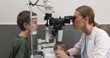 Modern oftalmoloji kliniğinde küçük bir çocuk için göz muayenesi yapmak için kesik lamba biyomikroskobu kullanan beyaz önlüklü profesyonel kadın optometrist. Teknoloji kullanarak gelişmiş göz sağlığı teşhisleri