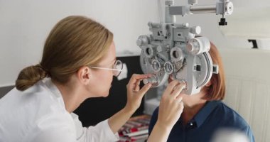 Modern oftalmoloji kliniğinde profesyonel phoropter kullanan yaşlı kadın hasta için vizyon muayenesi yapan genç bir kadın. Tıbbi göz kontrolü ve göz bakımı hizmetleri, kapatın.