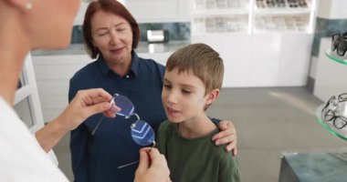 Gözlükçü, küçük sevimli çocuk için gözlük ayarlarken büyükannesi de gözlük dükkanında ona özenle ve destekle bakıyor. Vizyon bakımı, profesyonel hizmetler, çocuklar ve yaşlılar için düzenli kontroller