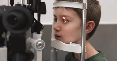 8 yaşındaki sevimli çocuğun göz muayenesi ve kesik lamba mikroskobu, parlak ışık demetini kapatması göz bebeğini yansıtırken, optometrist retina sağlığını inceliyor. Kontrol ve erken görüş bakımı