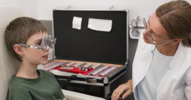 Modern oftalmoloji kliniğinde göz muayenesi sırasında deneme çerçevesi takan neşeli 8 'li yaşlarda sevimli bir çocukla çalışan pediatrik optometrist. Çocuklarda erken görme düzeltmesi ve göz sağlığı izleme