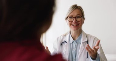 Beyaz önlüklü çekici bayan doktor soruları cevaplıyor, konuşma yapıyor, açıklama yapıyor ve sağlık tavsiyeleri veriyor, hasta omzunun üzerinden görüş açısını kapatıyor. Profesyonel tıbbi danışmanlık, sigorta.