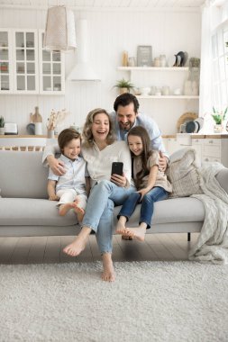 Dijital ebeveynlik. 4 çocuklu mutlu bir aile babası, iki farklı küçük çocuk kardeş rahat bir stüdyoda kanepede sarılıp gülüyor video araması yapıyor telefonda eğitim oyunu oynuyor.