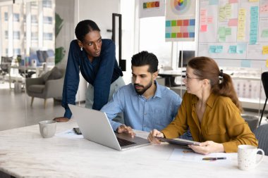 Dizüstü bilgisayarla konuşan, internet pazarlama stratejisi, çevrimiçi proje planı, takım çalışması için toplantı, toplantı odasında işbirliği yapan çok ırklı genç meslektaşlardan oluşan bir ekip.
