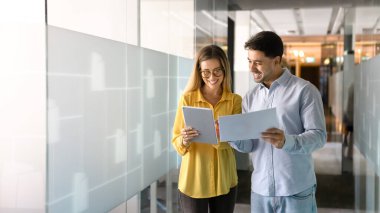 Ofis koridorunda birlikte yürürken elektronik ve kağıt raporlarını tartışan, tablet kullanan, belgeleri analiz eden, birbirlerine danışan, gülümseyen iki farklı iş adamı.