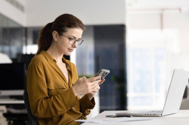 İş yerinde akıllı telefondan yazı yazan, internetten sohbet eden, mesajlaşan, internette gezinen, iş yerinde laptopla sosyal medya kullanan genç bir ofis çalışanı.