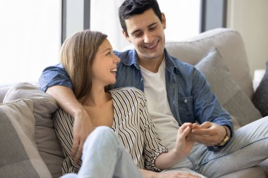 Mutlu genç çift oturma odasında rahat bir koltukta oturuyor, gülümsüyor ve el ele tutuşuyor, gündelik sohbetlerin keyfini çıkarıyor, hafta sonu aktiviteleri planlıyor, evde birlikte vakit geçiriyorlar. Romantik ilişki