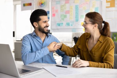 Mutlu yeni iş ortakları ofis masasında kağıt sözleşmesi imzaladıktan sonra el sıkışıyor, ortaklık kuruyor, işbirliği yapıyor, birlikte çalışıyor, anlaşma yapıyor, takım çalışmasından keyif alıyor.