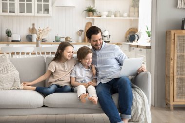 Dizüstü bilgisayarla eğlenmeyi öğreniyorum. Gülümseyen baba, interaktif eğitim uygulaması aracılığıyla iki farklı çocuğa kucak açıyor. İnternette oyun bilimi dersi veren komik videoları dizüstü bilgisayarda gösteriyor.