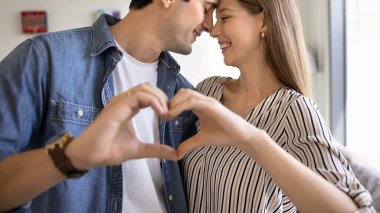 Sevecen bir çift birbirine yakın durur, alınlarına nazikçe dokunur ve elleriyle kalp şeklini oluşturur. Aşkın sembolü, romantik ilişkiler, Sevgililer Günü kutlaması, nişan