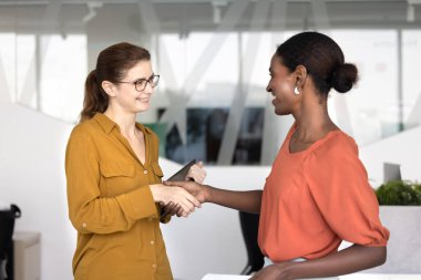Pozitif çoklu etnik kökenli yeni başlayan kadın meslektaşlar ofis alanında el sıkışıyorlar, çalışma alanında duruyorlar, selamlaşıyorlar. Afrikalı yönetici iş arkadaşına yardım, destek ve tavsiyeleri için teşekkür etti