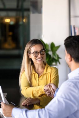 Cheerful young business professional woman in glasses getting hired, promoted, shaking hands with male colleague, boss, employer, thanking expert, consultant for help. Vertical shot