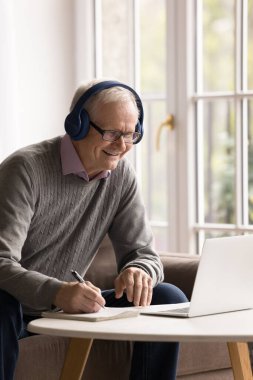 Yaşlandıkça tutkuyla öğreniyorum. Hevesli gülümseyen, dijital kulaklıklı yaşlı erkek emekliler, online bilgilerden esinlenerek dizüstü bilgisayarla evde sanal eğitim sınıfı web sitelerine katılıyorlar.
