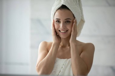 Çok temiz ve taze. Havluya sarılı heyecanlı genç bayan banyo prosedürlerini yenilettikten sonra avuçlarla yüze dokunmak ayna yansımasında yumuşak nemlendirilmiş parlak cildin mükemmel durumunu takdir eder.