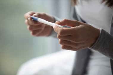 Evde test yapıyoruz. Kapalı genç kadın elleri taşınabilir hamilelik testi tutuyor. Aile planlaması erken teşhis doğurganlık yumurtlama ivf kişisel seçim kavramı