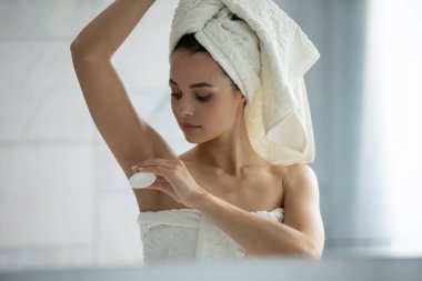 Duştan sonra zinde kalmak. Kafa vuruşu yapan mutlu genç bayan ev tuvaletindeki aynanın yanındaki koltuğun altına cilt dostu katı deodorant sür. Kişisel bakım tazelenmiş taze kokunun tadını çıkar.