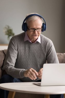 Yetişkin erkek, emekli, uzaktan kumandalı öğretmen öğrenci dijital kulaklık takıyor. Telekonferans üzerinden iş görüşmeleri yapıyor. İnternetteki sanal etkinlikte not defteri kullanarak iş projesini tartışıyorlar.