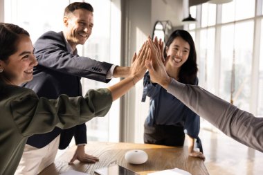 Dört başarılı iş arkadaşı grup beşliğini toplantı masasının üzerinde yapıyor. Takım başarısı, takım çalışmasının başarısı, büyük önemli görevin tamamlanması jestleri yapıyorlar.