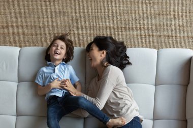 Asyalı anne ve oğulun rahat koltukta birlikte uzanması, gülen genç anne ve 7 'lerin çocukları eğlenceli aktiviteler, hafta sonları evde boş vakit geçirmeleri, ailelerinin eğlenmesi.