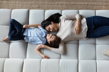 Gülen Asyalı anne ve oğlu eğleniyorlar, rahat koltukta birlikte uzanıyorlar, gülümsüyorlar genç anne ve 7 'nin çocuğu tembelliğin tadını çıkarıyorlar, hafta sonu, annelik kavramı.