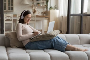 Büyük kulaklıklarda mutlu öğrenci kız öğrenci çevrimiçi sanal sınıf, atölye, dizüstü bilgisayar, yabancı dil eğitimi, öğretmenle video görüşmesi, özel ders, kanepede dinlenme.
