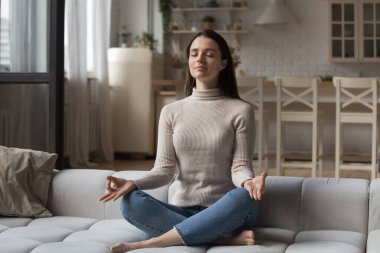 Huzurlu, sakin, milenyum Yogası kızı. Ev kanepede gözleri kapalı meditasyon yapıyor. El zen parmaklarını, dingin yüzünü, yoga yapıyor, zihin egzersizi yapıyor.