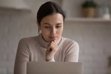 Evde çalışan düşünceli serbest çalışan bir kadın, dizüstü bilgisayarda metin okuyan, e-posta ve çevrimiçi proje üzerinde düşünen. Düşünceli öğrenci kız internette çalışıyor, Webinar izliyor.