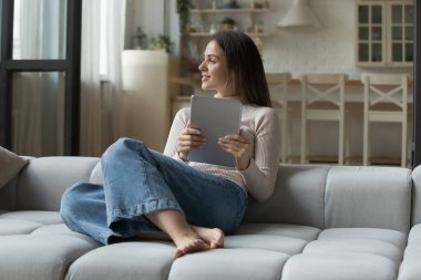 Mutlu rüya gibi alet kullanıcı kız dijital ped tutuyor, koltukta dinleniyor, düşünceli bir gülümsemeyle güzel düşünceler içinde başka tarafa bakıyor. Genç bir kadın, tablet bilgisayarda kitap okuyan, evde boş vakitlerin tadını çıkaran bir öğrenci.