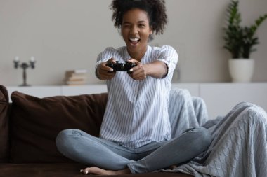 Mutlu genç milenyum siyah kız evde video oyunu oynuyor, joystick kullanıyor, evde kanepede oturuyor, sanal savaşta kavga ediyor, eğleniyor, sanal internet aktivitelerinden zevk alıyor..