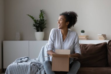 Mutlu genç Afrikalı kadın, milenyum alışverişçisi, çevrimiçi mağaza müşterisi evde karton kutuyu açıyor, internet dükkanından gelen paket paketini açıyor. Kutuları açmak, gülümsemek. Nakliye kavramı