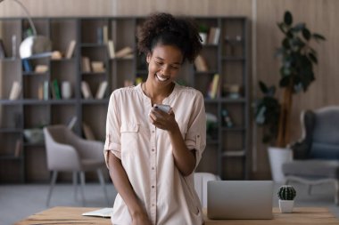 Mutlu genç Afrikalı kız akıllı telefon ekranında komik mesajlar okuyor, video izliyor, video görüşmeleri yapıyor, sosyal medyada sohbet ediyor, çöpçatanlık hizmetlerinde flört ediyor, uygulama kullanıyor.