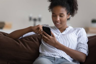 Mutlu, rahat, genç siyah kız, kanepede dinlenen kadın, boş vakitlerin tadını çıkaran, akıllı telefon uygulaması kullanan, kitap okuyan, telefon eden, video izleyen, internette gezinen.