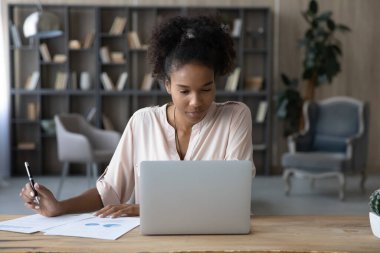 Evden dizüstü bilgisayarda çalışan odaklanmış Afrikalı uzaktan kumandalı bir çalışan istatistik raporlarını analiz ediyor. Öğrenci kız çevrimiçi pazarlamayı öğreniyor, Webinar izliyor, bilgisayar üzerinde sanal eğitim alıyor.