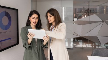 Ofiste işbirliği yapan iki profesyonel kadın, dijital tabletle ilgili verileri analiz ediyor, üretken bir takım çalışması ve stratejik planlama yapıyor. Karar verme mekanizması için teknoloji kullanımı, yeni yapay zeka uygulaması öğrenimi