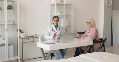 Doktor, orta yaşlı hastaya tıbbi bilgi ve test sonuçlarını, semptomları, tedavi planını veya bir sonraki teşhis adımlarını tartışarak, klinik ziyareti sırasında profesyonel sağlık tavsiyeleri vererek açıklıyor.