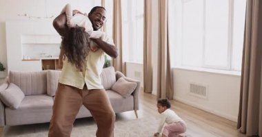 Modern oturma odasında iki melez kızla aktif oyunlar oynayıp dans eden siyah babayı sevmek. Neşeli bir aile, evde küçük mutlu çocuklarla eğlenip, kaygısızca vakit geçirmeyi sever.