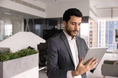Takım elbiseli Arap işadamı tablet cihazını kullanarak çevrimiçi çalışıyor, yeni işletme yapay zeka uygulamasını veya platformunu inceliyor, borsa eğilimlerini izliyor, dijital verileri analiz ediyor veya bilgi alıyor