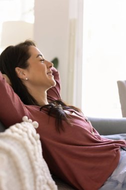 Tatmin olmuş çekici Latin kadın, kollarını başının arkasında dinlendirirken, tatillerde parlak, rahat bir evde ya da otel odasında gözleri kapalı gülümsüyor. Rahatlık, rahatlık ve huzur.