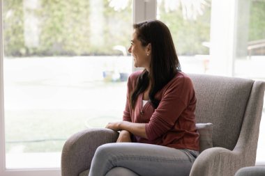 Kadın rahat koltukta rahatlıyor, oturma odasındaki büyük pencereden dışarı bakıyor, evde boş vaktini geçiriyor, hoş düşünceler içinde, nostaljik bir ruh halinde, evin içinde huzurlu bir anın tadını çıkarıyor.