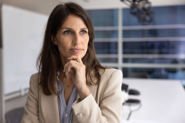 Modern konferans odasında düşünceli bir şekilde duran, çenesine dokunan, mesafeye bakan, plan yapan ya da karar veren 40 'lı yaşlarda orta yaşlı bir iş kadını. Stratejik düşünme, liderlik, iş dünyasında vizyon