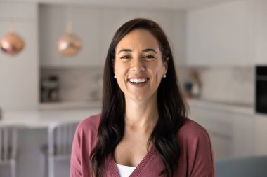 Gayrimenkul acentesinin portresi modern oturma odasında duruyor, kameraya olumlu bir ifadeyle bakıyor, profesyonel hizmetleri temsil ediyor, güven ve güvenilirlik yayıyor.