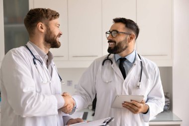 Başarılı bir tıbbi işbirliği. İki gülümseyen doktor, modern klinik ofisinde, dijital kağıt kayıtları kullanarak hasta davasında verimli bir ekip çalışması yaptıktan sonra mesleki ortaklık kurdular.