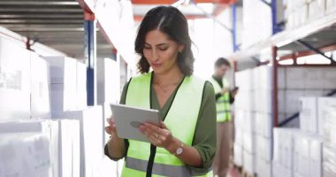 Teslimattan sonra malları sayan, lojistik kutuları kontrol eden, tablet bilgisayardaki elektronik yol faturalarına danışan, envanter yapan, sarı yelekli, genç İspanyol kadın depo yöneticisi.