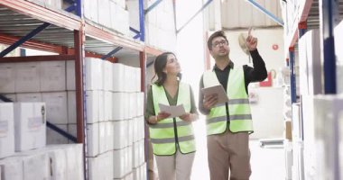 Latin denetçi adam müfettiş kadına depoyu gösteriyor. Erkek depolama müdürü yeni çalışan, stajyer, lojistikten, ticaretten bahsediyor, raflardaki istiflenmiş kutuları gösteriyor.