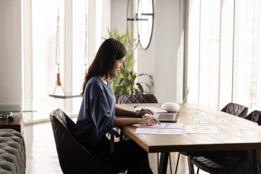 Ürün açılışı için internet pazarlama stratejisi üzerinde çalışan meşgul genç Asyalı kadın, ofis işyerindeki dizüstü bilgisayarda yazı yazma, kağıt istatistik satış raporlarını analiz etme