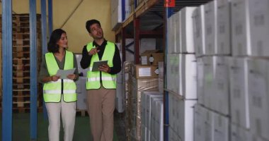 Depo amiri, depo düzenleyicisinden kadın çalışana, patron ve yeni çalışana gösteriyor. İki Latin meslektaşı depoda yürüyor, ellerinde tablet ve belgeler var.